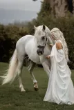 Fine art equine portrait of a white horse walking beside a woman in flowing white gown at Usk Castle, captured by Sharon Byrne Photography in Ireland