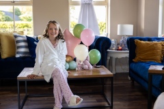 Fun portrait of Willow sitting beside balloons and her First Communion dress at home.
