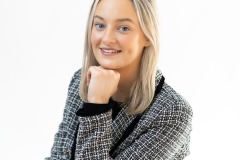 Professional headshot of Sarah, smiling confidently in a checkered blazer, photographed in a bright studio setting.