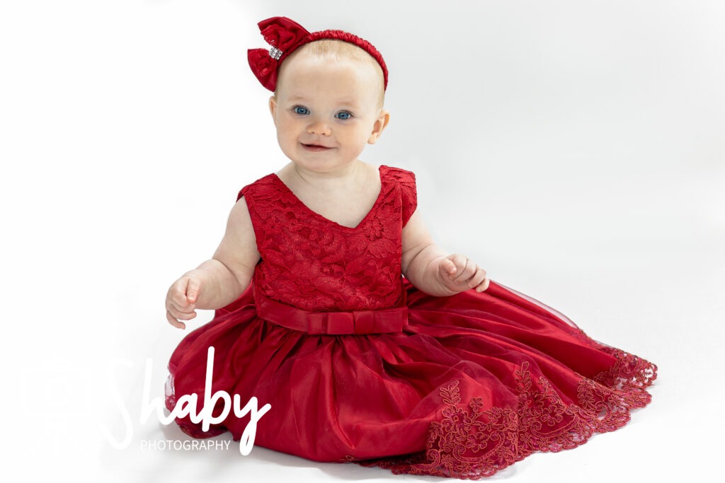 Close-up of toddler Nina posing in a bright red dress for a playful photography session