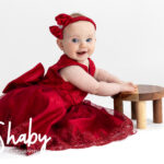 Close-up of toddler Nina posing in a bright red dress for a playful photography session