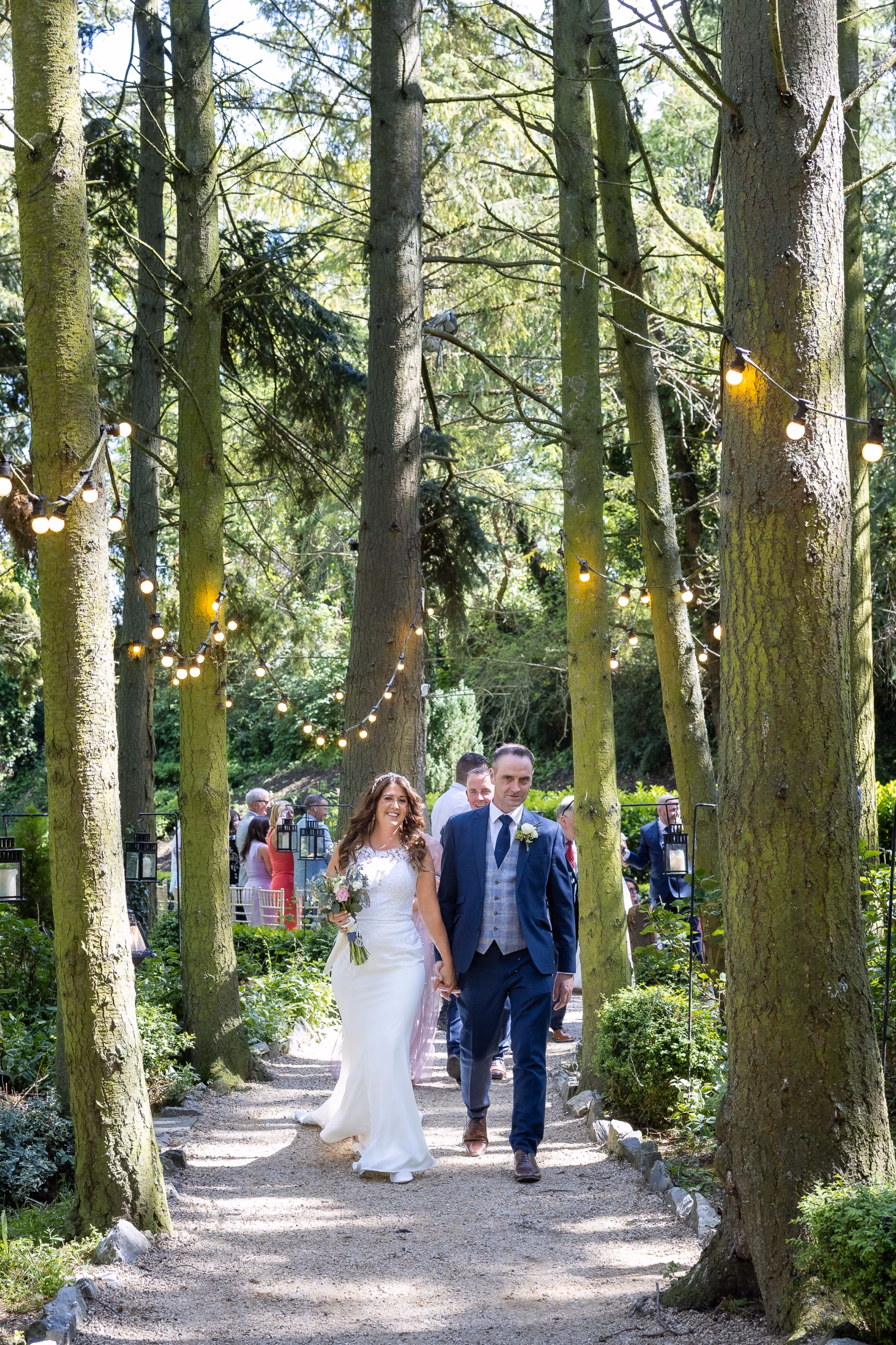 Photo of Edel and Davy, the bride and groom, holding hands and walking back through the woods after their beautiful wedding ceremony