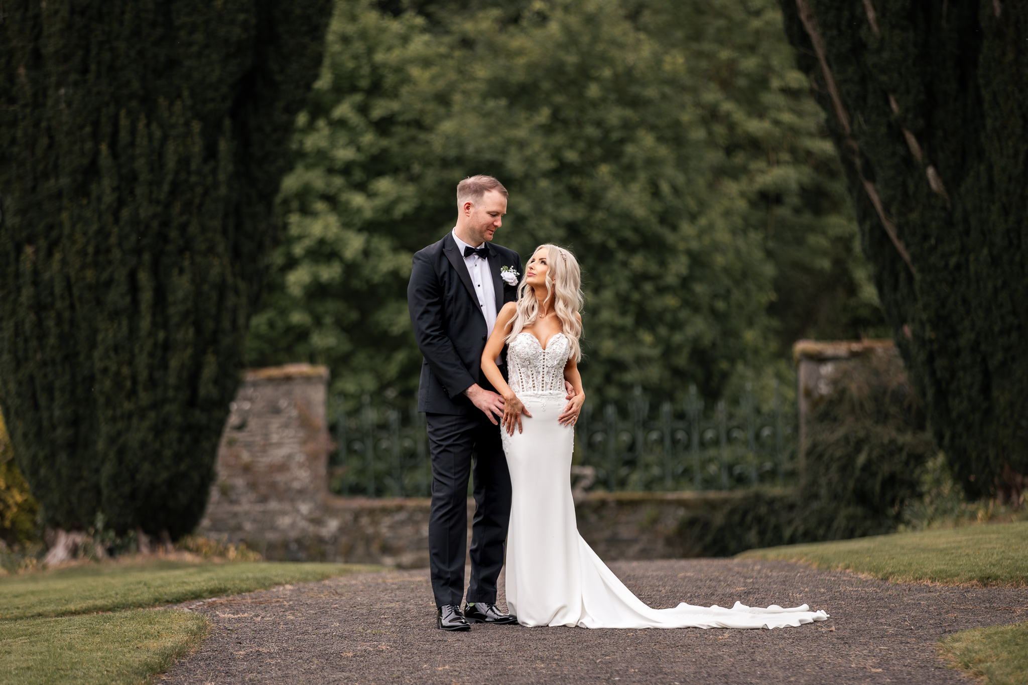 Bride and groom embracing face to face on a path lined with tall green hedges