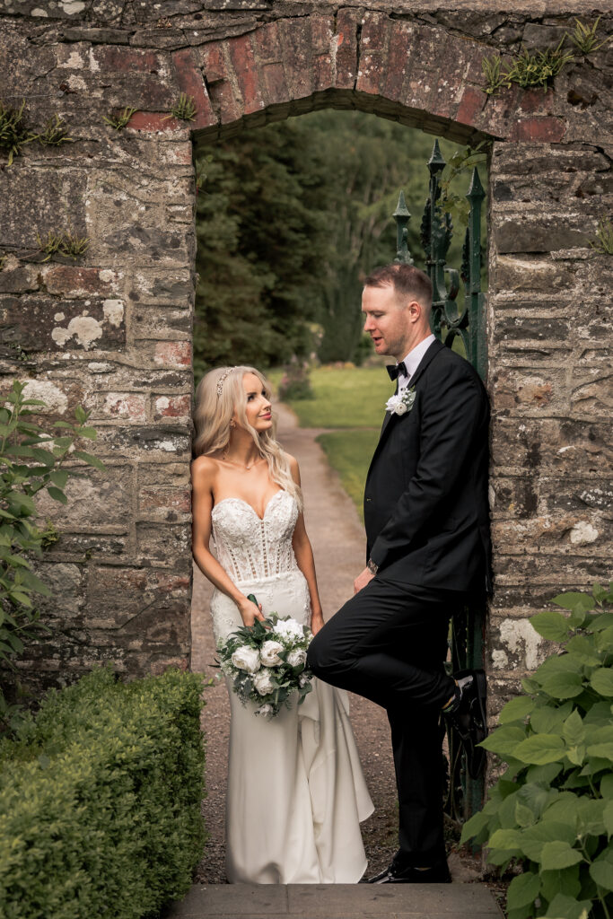 Bride and groom in a weathered stone archway, groom leaning beside the bride