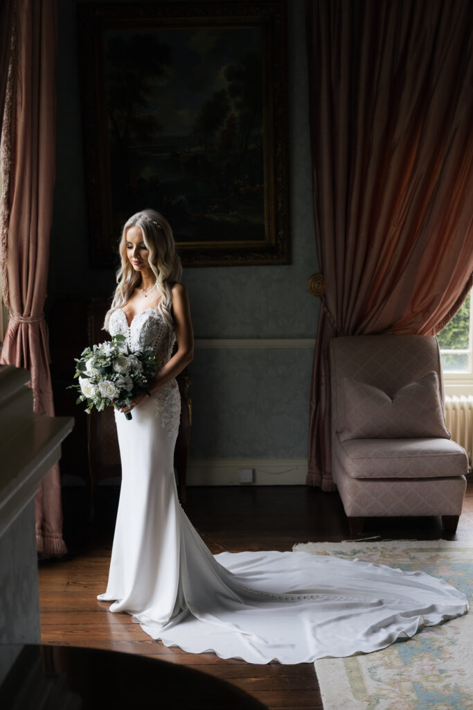Bride holding a bouquet in an elegant room with heavy drapes and a classic painting