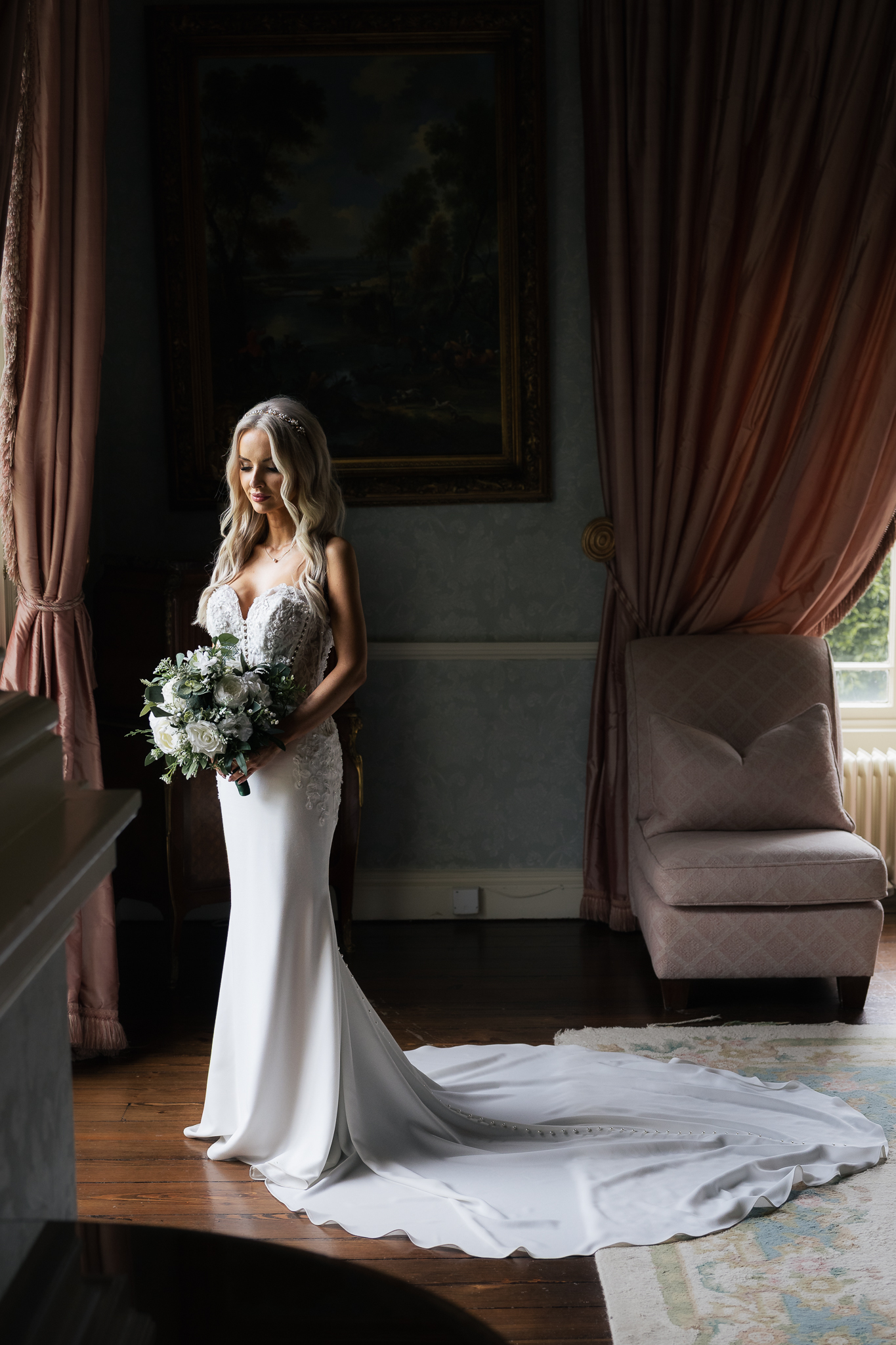 Bride holding a bouquet in an elegant room with heavy drapes and a classic painting