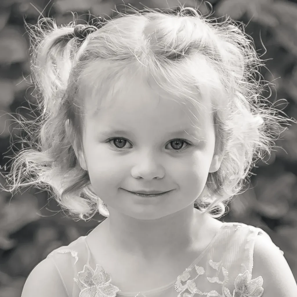 Black and white close up portrait of a two year old girl with backlit curly hair, smiling at the camera