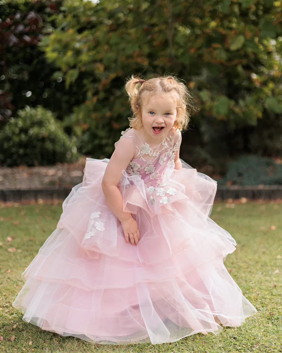 Two year old girl twirling on the lawn in a long pale pink princess dress