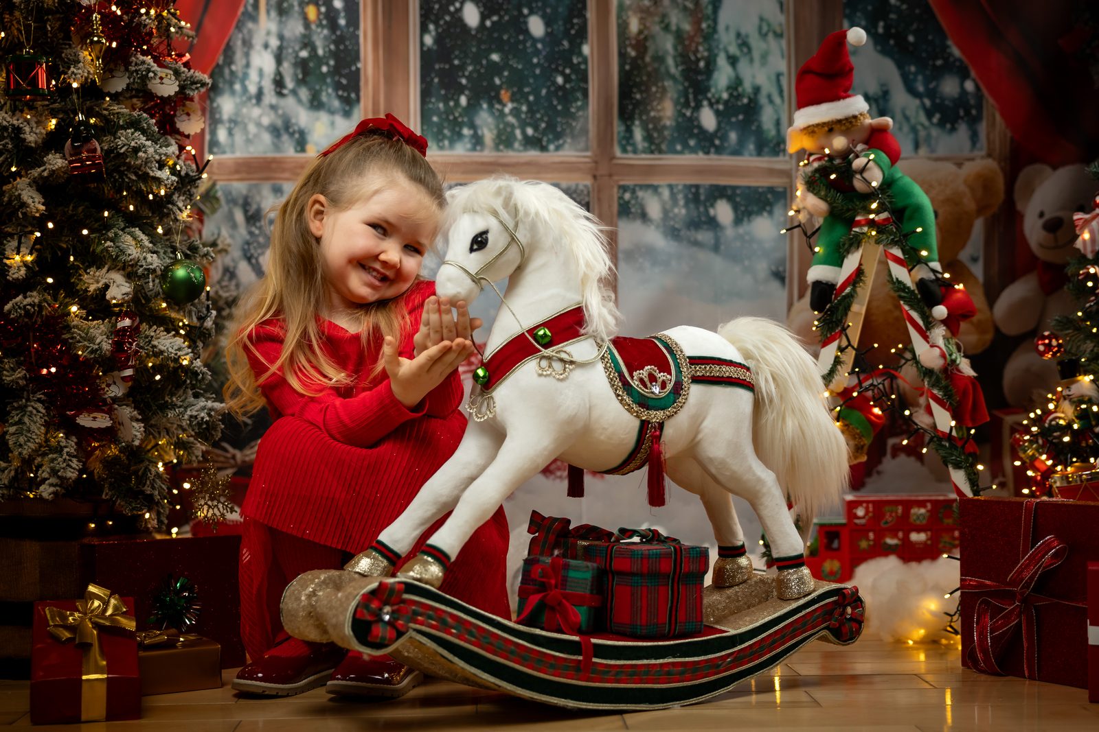 Young girl laughing beside a white rocking horse in a Christmas studio set