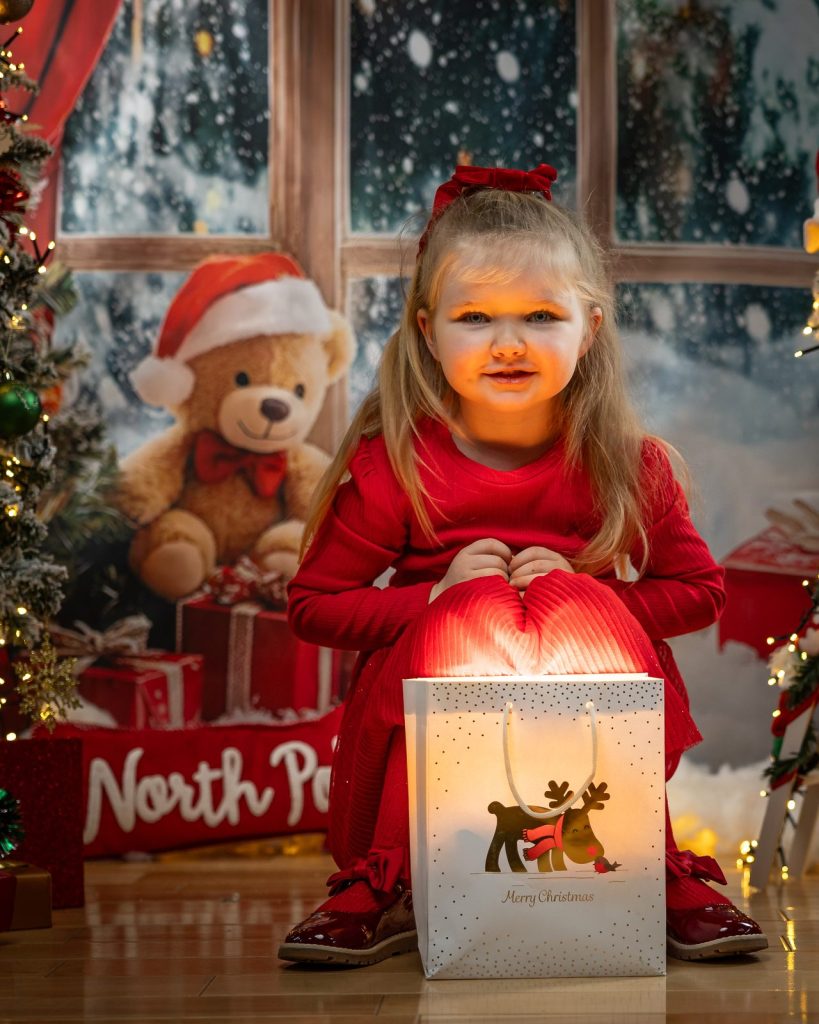 Girl lit by the warm glow of a Merry Christmas gift bag in a snowy window set