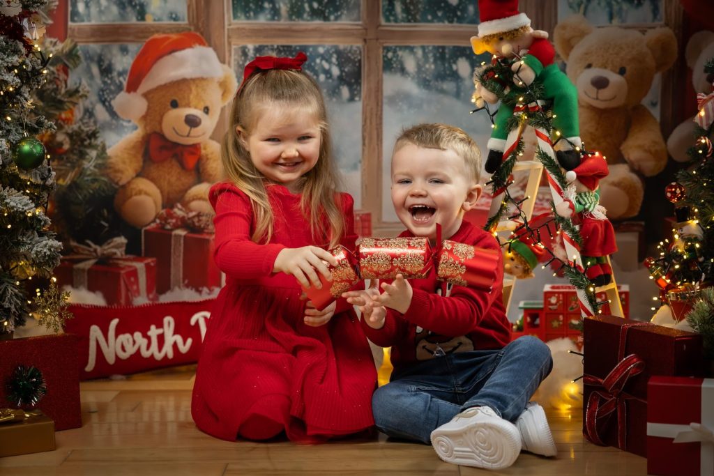 Brother and sister laughing as they pull a Christmas cracker in a festive studio set, Meath
